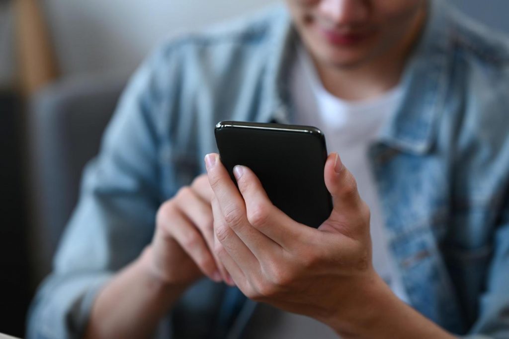 caption: Cropped shot young man using a smartphone for checking social media ordering delivery at home.