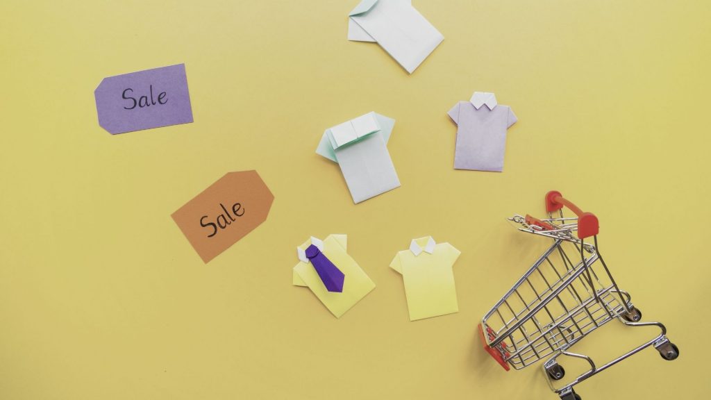 Image of scattered paper shirts near shopping trolley and sale tags